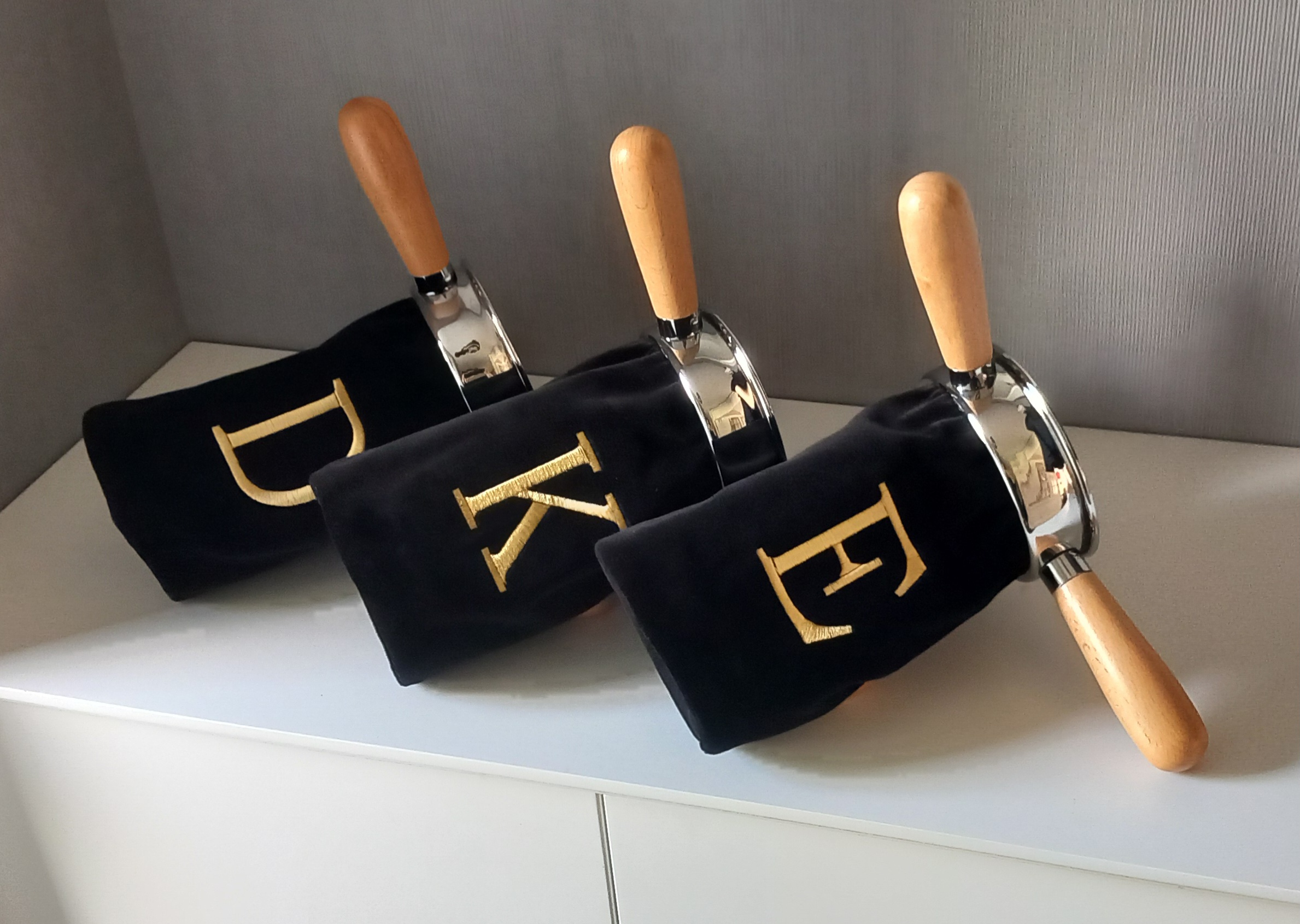 Zwarte collectezakken met beuken houten handgrepen en goud geborduurde letters D (Diaconie), K (Kerk) en E (Extra collecte).