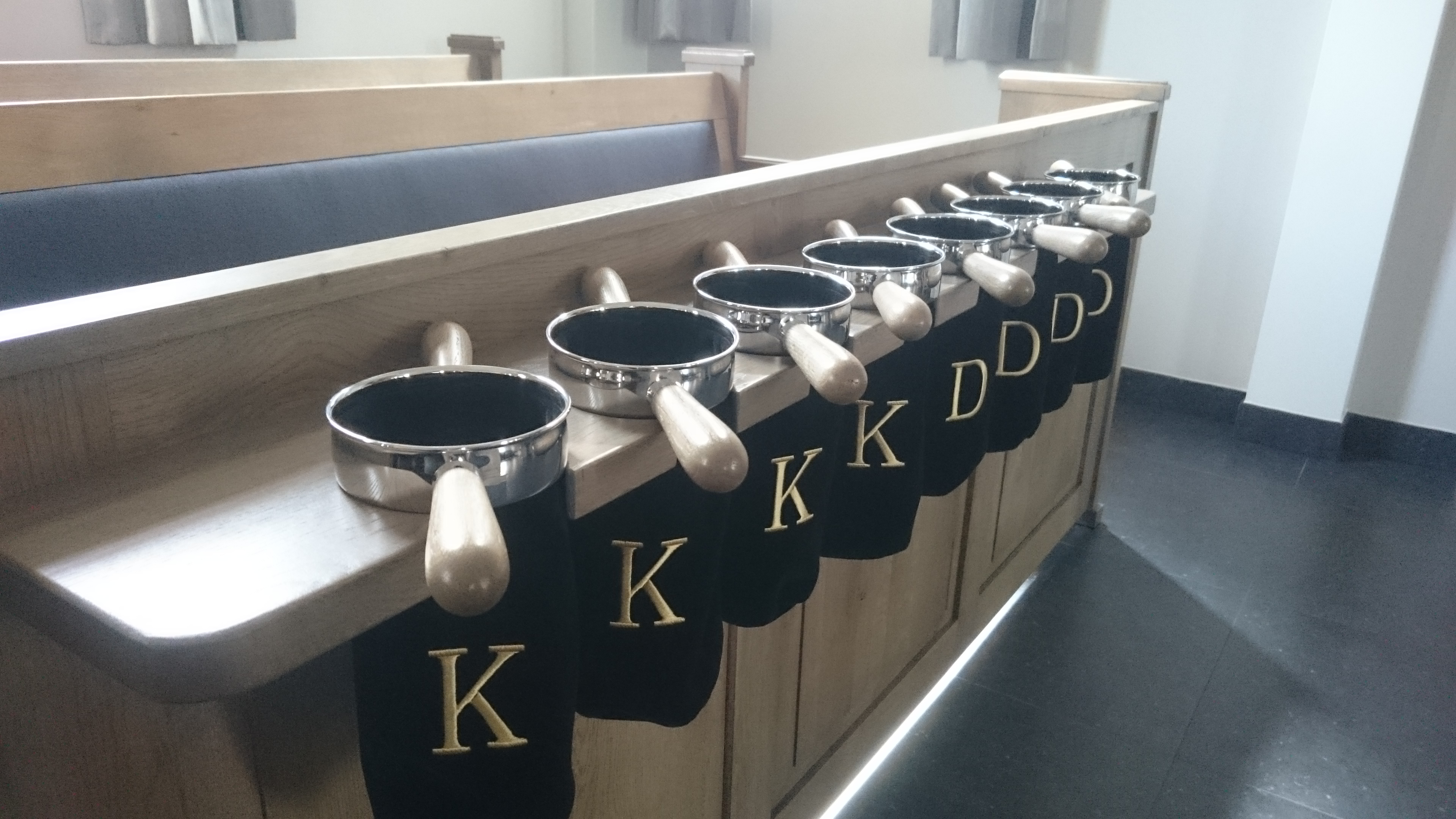 Zwarte collectezakken met goud geborduurde letters K (Kerk) en D (Diaconie) in een collectezakrek.